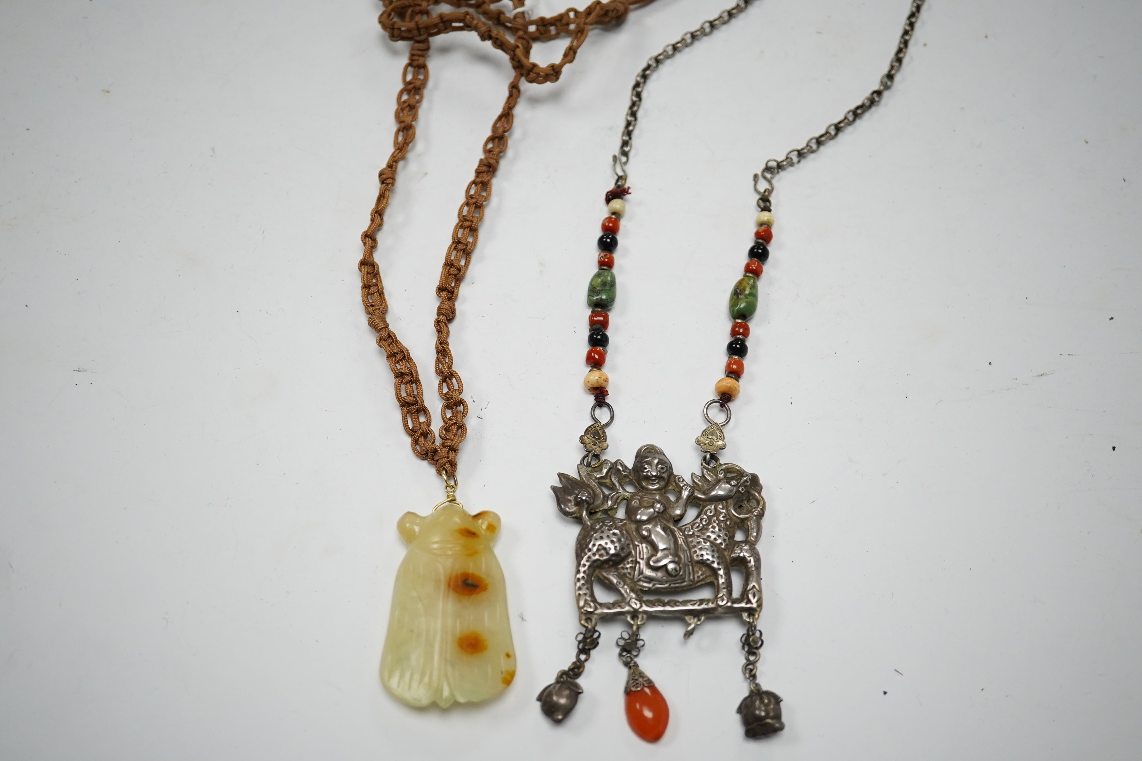 A Chinese celadon and russet jade cicada pendant on cording and a silver and stone mounted chain and pendant of boy riding a qilin, cicada 5.5cm long (2). Condition - tip of cicada wing chipped and on silver pendant one